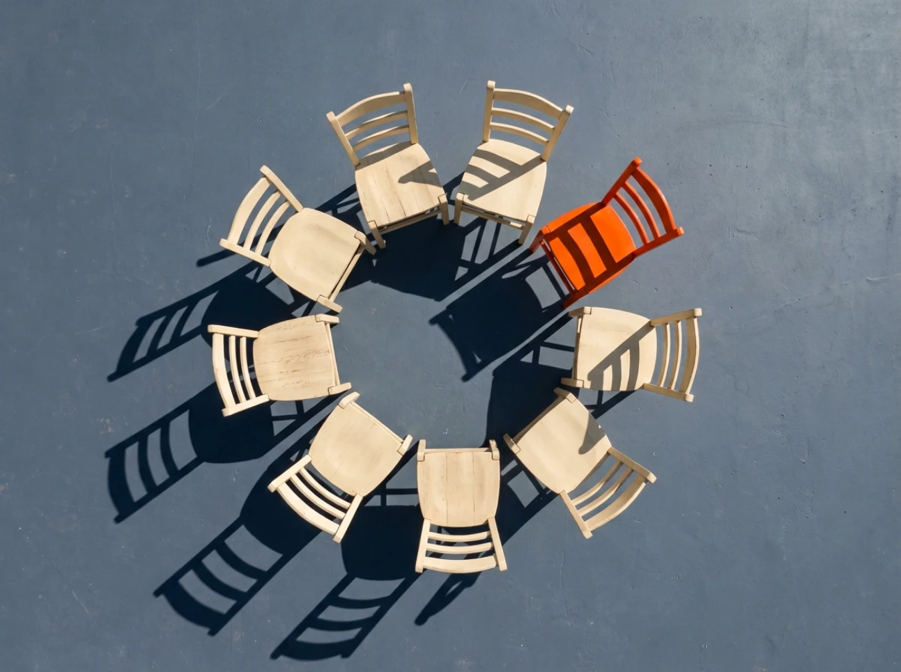 Circle of wooden chairs with one orange chair on slate floor